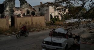 A man drives his motorcycle past a destroyed car in the retaken village of Velyka Oleksandrivka, Ukraine, Wednesday, Oct. 12, 2022. 