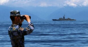 A People's Liberation Army member looks through binoculars during military exercises as Taiwan frigate Lan Yang is seen at the rear, on Friday, Aug. 5, 2022.