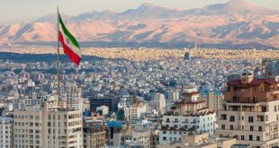 Waving Iran flag above skyline of Tehran at sunset. 